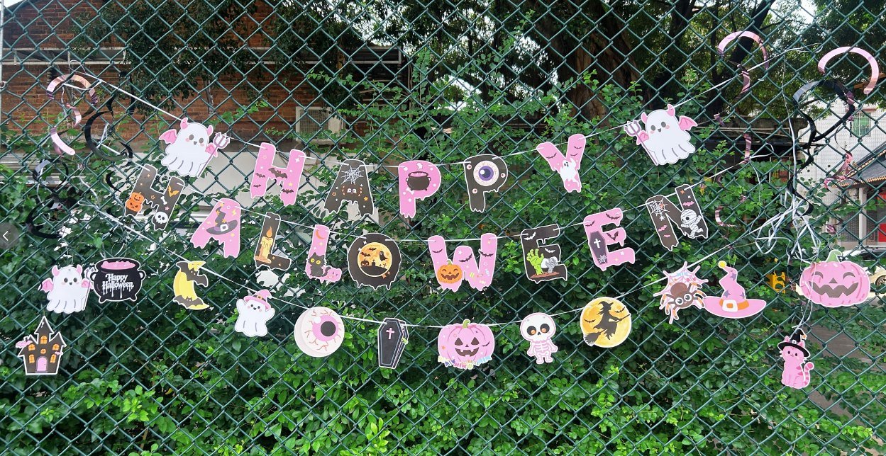 Pink Halloween party decoration set displayed outdoors on a fence — Happy Halloween banner and hanging character cutouts