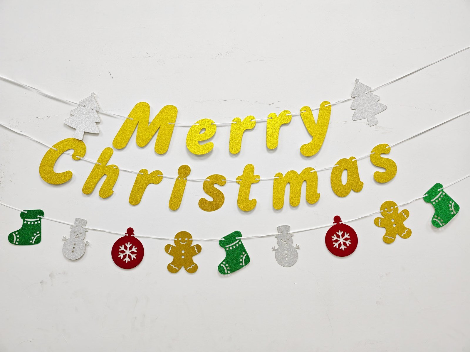 Christmas glitter banner set Style 2606 hung on a wall — gold glitter lettering with stocking, snowman, bauble and gingerbread motifs